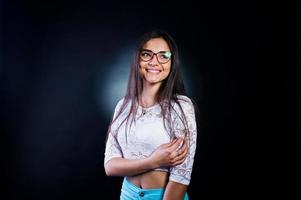 portrait d'une jolie jeune femme en haut blanc et pantalon bleu posant avec ses lunettes dans le noir. photo