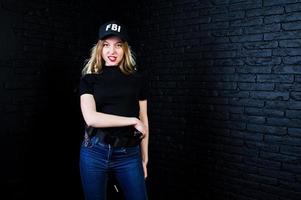 agent féminin du fbi en casquette et avec arme à feu au studio contre un mur de briques sombres. photo