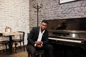 fort puissant homme afro-américain en costume noir assis contre le piano. photo