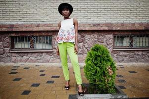 incroyable femme modèle afro-américaine en pantalon vert et chapeau noir posé à la ville. photo