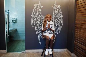 belle femme africaine dans des vêtements décontractés élégants posant contre le mur des ailes d'ange. photo