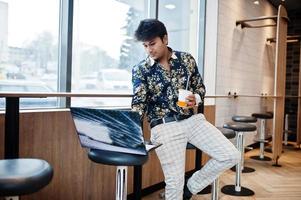 jeune homme indépendant indien assis sur un ordinateur portable ouvert dans un café de restauration rapide, bel homme asiatique lisant un message texte pendant le travail sur net-book dans un café confortable. photo