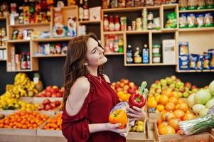 fille en rouge tenant différents légumes sur le magasin de fruits. photo