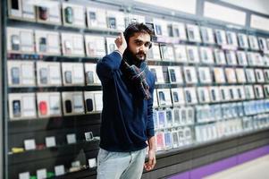 Acheteur client homme barbe indien au magasin de téléphonie mobile avec écouteurs sans fil. concept de peuples et de technologies d'asie du sud. magasin de téléphonie mobile. photo