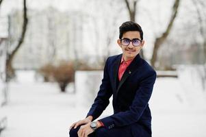 homme étudiant indien élégant en costume et lunettes posé à la journée d'hiver en plein air. photo