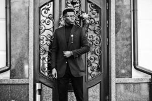 un homme afro-américain à la recherche étonnante porte un blazer bleu avec une broche, un col roulé noir et des lunettes posées dans la rue. mec noir à la mode. photo