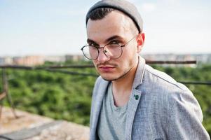 homme macho élégant rêveur en costume gris, chapeau et lunettes posés sur le toit. photo