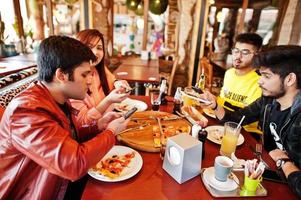 groupe d'amis asiatiques faisant des photos de pizza par téléphone lors d'une fête à la pizzeria. des indiens heureux s'amusant ensemble, mangeant de la nourriture italienne et assis sur un canapé.