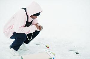 pêcheur afro-américain avec canne à pêche assis sur la mer gelée. pêche d'hiver. photo