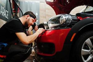 le travailleur du service automobile a mis un film anti-gravier sur une carrosserie de voiture rouge à l'atelier de détail du véhicule. protection de voiture avec des films spéciaux. photo