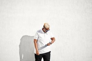 garçon musulman arabe élégant avec à l'origine des cheveux et des lunettes de soleil posés dans les rues au toit contre le mur blanc. photo