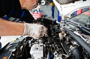 thème de la réparation et de l'entretien des voitures. mécanicien en uniforme travaillant dans le service automobile, vérifiant le moteur. photo