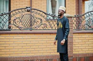 homme africain riche en vêtements traditionnels élégants et chapeau posé sur fond extérieur son manoir. photo