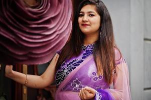 fille hindoue indienne au sari violet traditionnel posé dans la rue près de la grande rose décorée. photo