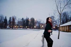 fille brune en pull vert et écharpe rouge en plein air le soir de la journée d'hiver. photo