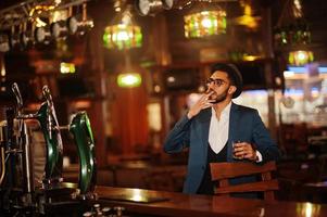 bel homme arabe bien habillé avec un verre de whisky et de cigare posé au pub. photo