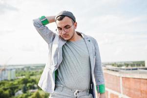 homme macho élégant rêveur en costume gris, chapeau et lunettes posés sur le toit. photo