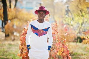 homme afro france élégant et branché en chapeau rouge et tenue blanche posée au jour de l'automne. gars modèle africain noir. photo