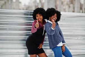 deux femmes afro-américaines aux cheveux bouclés portent des chandails posés le jour de l'hiver, montrent les pouces vers le haut. photo