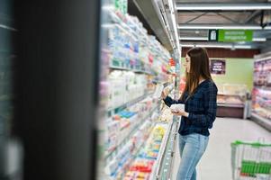 femme commerçante regardant les étagères du supermarché. portrait d'une jeune fille dans un magasin de marché tenant la production de lait. photo