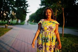 jolie fille afro-américaine de petite taille avec des dreadlocks, porter une robe jaune colorée, posée au coucher du soleil. photo