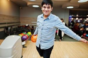 homme sud-asiatique en chemise jeans debout au bowling avec ballon sur les mains. guy se prépare pour un lancer. photo