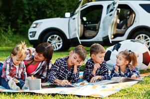 la famille passe du temps ensemble. mère avec quatre enfants en plein air dans une couverture de pique-nique contre leur suv américain. photo