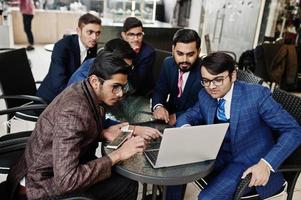 groupe de six hommes d'affaires indiens en costumes assis au bureau sur un café et regardant un ordinateur portable. photo