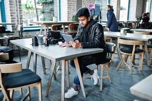 photographe de jeune homme asiatique intelligent travaillant avec une tablette pendant qu'il était assis au café. photo