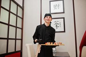 chef professionnel porter en noir avec des sushis et des petits pains dans un restaurant de cuisine traditionnelle japonaise. photo