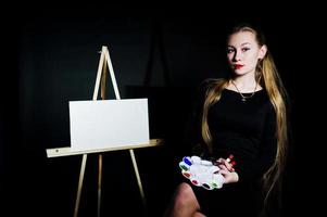 belle femme artiste peintre avec pinceaux et toile à l'huile posant en studio isolé sur noir. photo