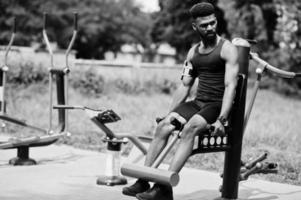 homme de sport afro-américain athlète masculin avec étui de bras de sport en cours d'exécution pour téléphone portable, faisant des exercices sur les simulateurs d'entraînement de rue. photo