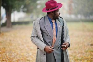 élégant modèle d'homme afro-américain en manteau gris, cravate de veste et chapeau rouge posé dans la rue par temps brumeux à l'automne. photo