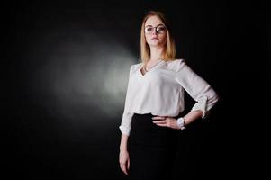 portrait en studio d'une femme d'affaires blonde à lunettes, chemisier blanc et jupe noire sur fond sombre. femme réussie et concept de fille élégante. photo