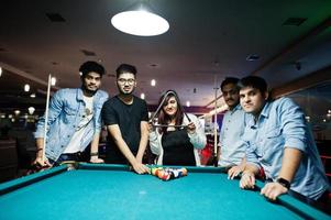 groupe d'amis asiatiques élégants portent des jeans jouant au billard au bar. photo