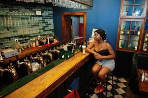 portrait d'une femme afro-américaine, coiffure rétro posant au restaurant sur le comptoir du bar avec une tasse de latte. photo