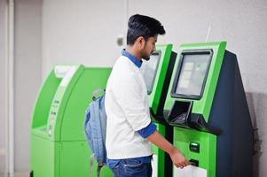 un jeune homme asiatique a mis sa carte de crédit pour retirer de l'argent d'un guichet automatique vert. photo