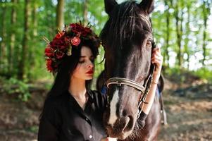 fille mystique en guirlande en noir avec cheval en bois. photo