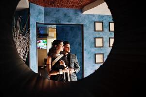 joli couple indien amoureux, porter au sari et costume élégant, posé sur le restaurant au cercle rond au mur. photo