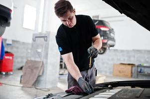 thème de la réparation et de l'entretien des voitures. mécanicien en uniforme travaillant dans le service automobile, vérifiant le moteur. photo