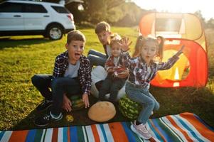 quatre enfants passent du temps ensemble. couverture de pique-nique en plein air, assis avec des pastèques. photo