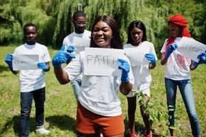 un groupe de volontaires africains heureux tient un tableau blanc avec un signe de foi dans le parc. concept de volontariat, de charité, de personnes et d'écologie en afrique. photo