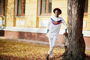 homme afro france élégant et branché en chapeau rouge et tenue blanche posée au jour de l'automne. gars modèle africain noir. photo