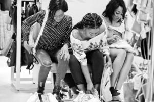 trois femmes africaines choisissant des vêtements au magasin. Jour de shopping. ils achètent des chaussures, sont assis sur un banc et portent des baskets. photo