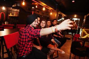 groupe d'amis indiens assis au bar-salon, s'amusant et se reposant, fumant du narguilé et regardant sur les téléphones portables pour faire du selfie. photo