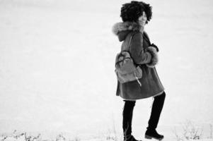 cheveux bouclés femme afro-américaine portant un manteau en peau de mouton et des gants avec sac à dos posés le jour de l'hiver. photo