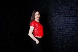 portrait d'une belle fille brune en t-shirt rouge et pantalon noir à côté du mur de briques du studio. photo