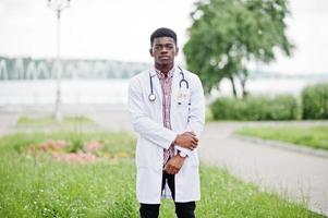 jeune médecin de sexe masculin afro-américain en blouse blanche avec un stéthoscope posé à l'extérieur. photo