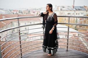 jolie fille indienne en robe sari noire posée au balkony. photo