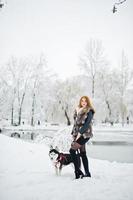 fille aux cheveux rouges marchant au parc avec un chien husky le jour de l'hiver. photo